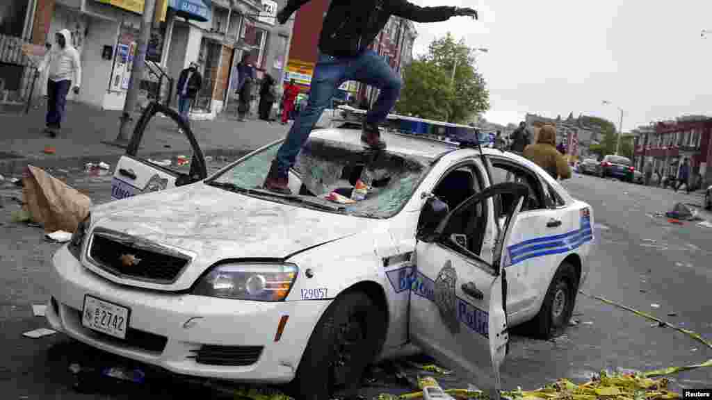 Один из участников уличных беспорядков в Балтиморе на поврежденной полицейской машине 