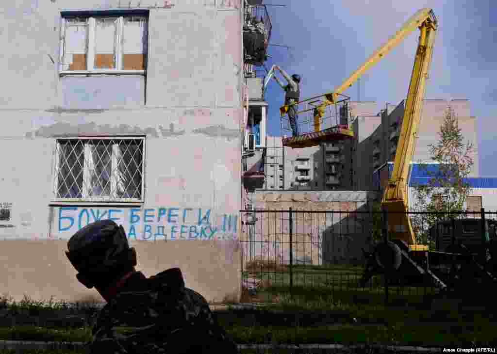 Пока ван Хелтен поднимается на рабочее место, украинский военный проходит мимо граффити: “Боже, береги Авдеевку”